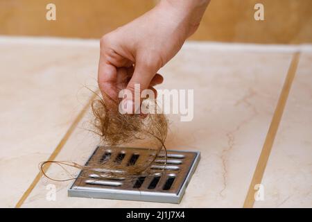 Donna che rimuove il pelo dal drenaggio della doccia Foto Stock