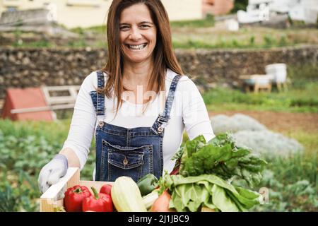 Donna contadina matura che tiene la scatola di legno con verdure fresche biologiche - Focus sul viso Foto Stock