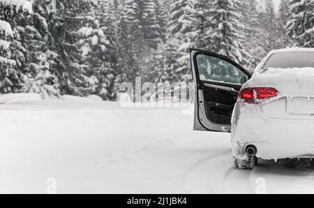 Auto argentata parcheggiata su strada invernale coperta di neve, porta d'ingresso aperta, sfondo di alberi sfocati, vista da dietro Foto Stock