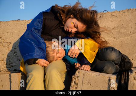 Civili, ucraini, rifugiati, un ragazzino e una giovane donna sono stanchi su blocchi di cemento, coperti da una bandiera Ucraina blu e gialla. Famiglia, u Foto Stock