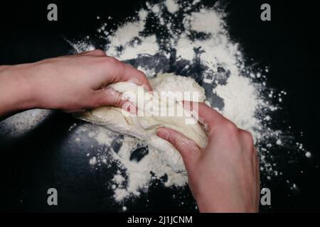 Pasta per pizza su un tavolo nero con le mani Foto Stock