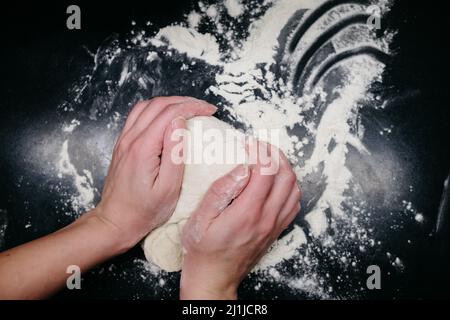 Pasta per pizza su un tavolo nero con le mani Foto Stock