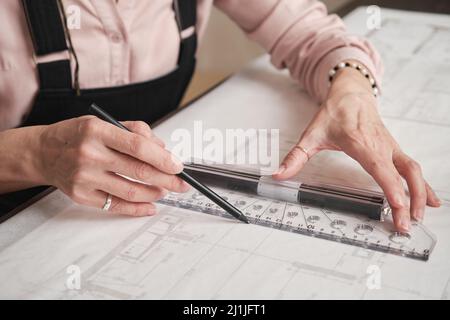 Primo piano di mani femminili inriconoscibili nell'anello usando righello e matita e creando disegno tecnico Foto Stock