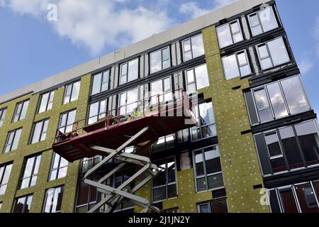 Pannello isolante esterno in lana di roccia installato sulla facciata del nuovo edificio da una piattaforma di sollevamento a forbice Foto Stock