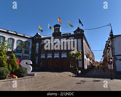 Vista della famosa piazza Plaza de la Constitucion nel centro storico di Arucas, Gran Canaria, Spagna con bandiere su vecchio edificio in giornata di sole. Foto Stock