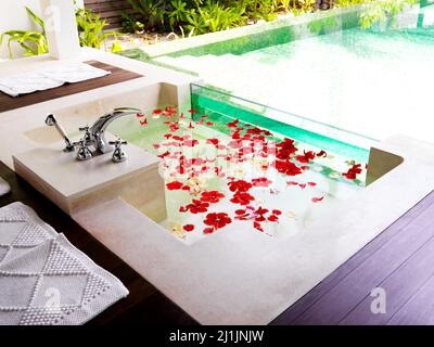 Pronto per il relax. Un moderno bagno con vasca piena di petali di fiori in un centro benessere. Foto Stock