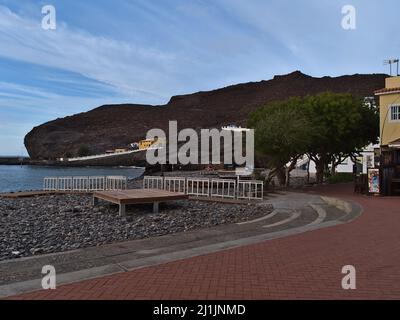 Vista della spiaggia di pietra di la Aldea de San Nicolas, Gran Canaria in serata con passeggiata, edifici e rocce nella stagione invernale. Foto Stock