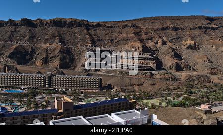 Vista aerea sul piccolo villaggio Taurito situato in una valle nel sud di Gran Canaria, Spagna con edificio alberghiero incompiuto sul pendio in giornata di sole. Foto Stock