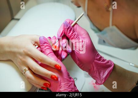 Primo piano del maestro manicure in guanti di gomma che applicano unghie rosse nel salone di bellezza. Foto Stock