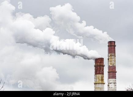 Fumo bianco spesso da fabbrica industriale vecchi camini arrugginiti su uno sfondo cielo grigio nuvoloso Foto Stock