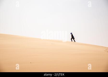 Un turista che arrampica una duna di sabbia in Azoueiga, Erg Amatlich, Regione di Adrar, Mauritania Foto Stock