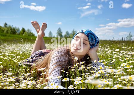 Donna felice spensierata sdraiata sul prato verde e godendo il sole sul suo viso. Ragazza che riposa nel parco primaverile. Godetevi la vita, divertirsi, divertirsi, rilassarsi Foto Stock