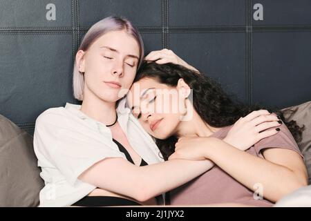 Giovane donna calma e amorevole con occhi chiusi abbracciando la ragazza mentre si trovano a letto Foto Stock