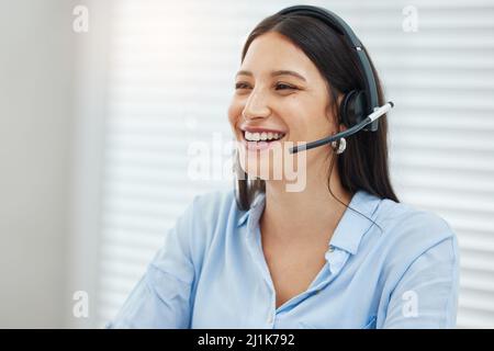 Fammi sapere come posso aiutarti. Scatto di una giovane donna di vendita seduta da sola nel suo ufficio e che indossa una cuffia. Foto Stock