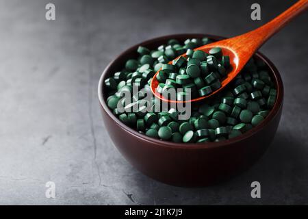 Compresse di spirulina organica in una tazza di legno con un cucchiaio di legno su sfondo scuro con vista dall'alto dello spazio libero Foto Stock