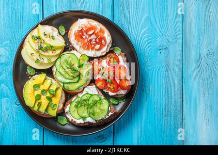 Diversi tipi di bruschetta con feta e ricotta su sfondo blu. Assortimento di sandwich. Foto Stock