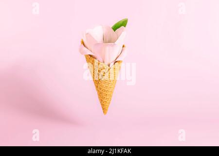 Concetto di iridamento minimo estivo. Cono di gelato volante con fiori di tulipano rosa su sfondo rosa. Concetto originale primavera per il compleanno, val Foto Stock