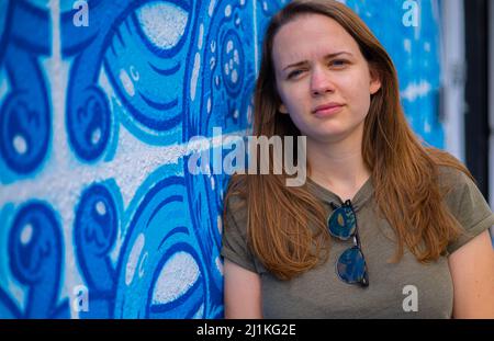 Giovane e bella donna si appoggia contro un muro colorato e si pone per la macchina fotografica - stile di strada tipico Foto Stock