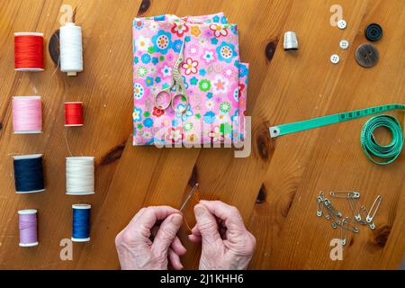 Mani della persona più anziana con artrite godendo cucire in uno stile piatto di posa surrrounded dagli accessori di cucito Foto Stock