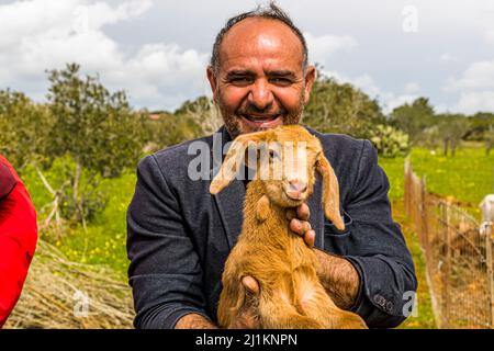 Agricoltore a Cipro del Nord con piccola capra Aleppo. La capra ha orecchie lunghe distintive. Nel nord di Cipro è allevato per la sua elevata resa di latte. Nel villaggio di Akdeniz, che tradotto significa Mar Mediterraneo, si ottiene un'impressione di vita tipica cipriota paese. Il sindaco Tarik mostra le capre che hanno solo un giorno di età Foto Stock