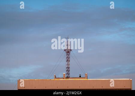 Antenna per telecomunicazioni installata sul tetto di un edificio moderno contro il cielo nuvoloso Foto Stock