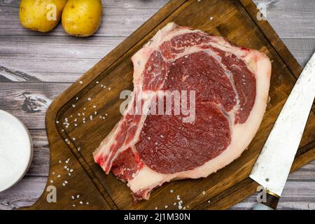 Una bistecca di osso o di osso o di porterhouse crudo su un tagliere su un tavolo di legno con una ciotola e sale. Vista dall'alto. Vista alta. Primo piano. Foto Stock