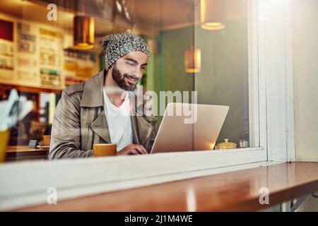 Come accedere al suo caffè locale. Scatto di un bel giovane seduto al bancone di un caffè utilizzando un computer portatile. Foto Stock