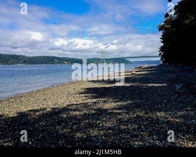 Spiaggia rocciosa di fronte con bel ponte in lontananza che si estende su massicce masse d'acqua. Foto Stock