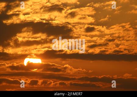Vista di un tramonto colorato in una serata di marzo con il sole che sbucciano dalla nuvola colorata di tramonto, alcune con fodere gialle dorate. Foto Stock