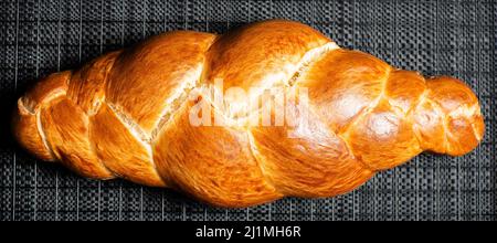 Bel pane dorato cotto a tre treccia con lavaggio delle uova. Challah è un pane speciale di origine ebraica Ashkenazi, solitamente intrecciato e consumato tipicamente Foto Stock