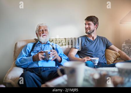 Trascorrere del tempo di qualità con il nonno. Shot di un uomo anziano e suo nipote adulto che si godono il caffè insieme sul divano a casa. Foto Stock