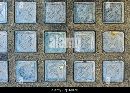 Una serie di piastrelle di vetro trasparente sono intarsiate in un pavimento di cemento Foto Stock