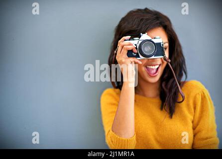 Buon serpente. Ritratto da studio di una giovane donna con una fotocamera vintage su sfondo grigio.