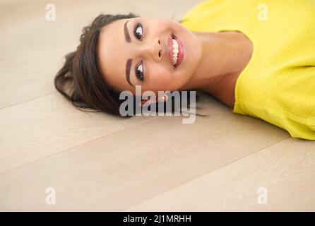 Accesso alla modalità relax.... Scatto corto di una giovane donna sdraiata su un pavimento di legno. Foto Stock