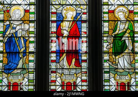 Una vetrata vittoriana che mostra le tre virtù teologiche fede, speranza e Carità come belle giovani donne. Faith legge un libro religioso Foto Stock