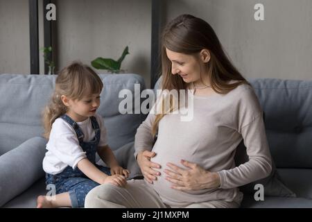 Madre felice che parla del bambino futuro con la figlia piccola. Foto Stock