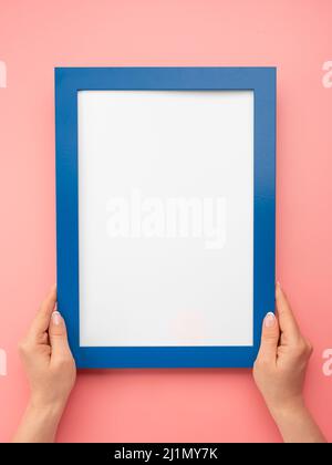 Donna tenere bianco diploma cornice su sfondo rosa parete. Le mani femminili tengono il telaio blu vuoto del mockup. Mano ritagliata di donna che tiene la cornice del diploma contro Foto Stock