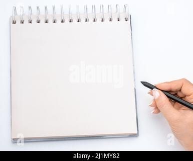 primo piano view femminile scrittura mani in mockup blocco note isolato su bianco. Donna che scrive in blocco note. Blocco note mockup con le mani della donna sul dorso del tavolo bianco Foto Stock