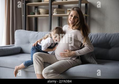 Ragazza piccola felice che mette l'orecchio sul ventre incinta. Foto Stock