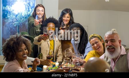Grande gruppo di persone che brinda ad una festa, amici felici che festeggiano un annuncio, festa di Natale con persone di tutte le età e nazioni Foto Stock