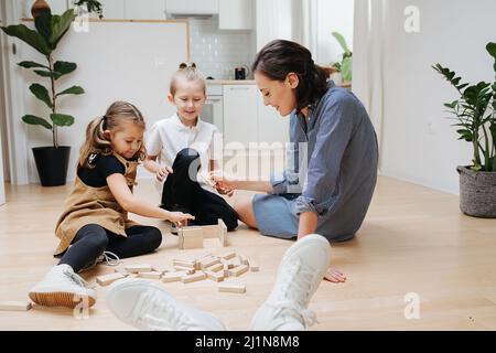 Giochi di famiglia felici sul pavimento. I piedi di papà nelle sneakers bianche in primo piano, lo guardano. Costruire cose da blocchi di legno. Foto Stock