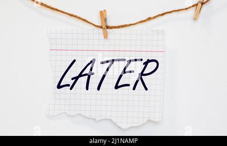 Uomo d'affari in miniatura seduto su penna e nota appiccicosa con la mano che scrive la parola più tardi su sfondo nero scuro usando come procrastination, pigro e posta Foto Stock