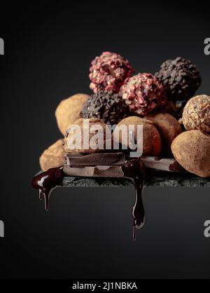 Deliziosi tartufi di cioccolato e gocce di salsa di cioccolato su sfondo nero. Foto Stock