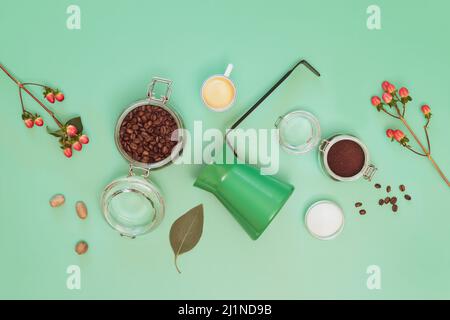 Preparazione del caffè. Composizione delle bevande con chicchi di caffè, caffè macinato, zucchero, tazza di espresso, caffettiera turca e fiori su sfondo menta. Piatto l Foto Stock