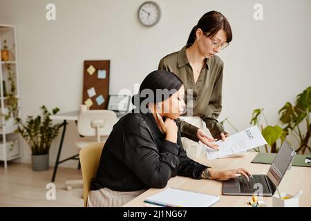 Ritratto laterale di due donne d'affari di successo che discutono i documenti di lavoro in ufficio minimo Foto Stock