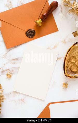 Autunno ancora vita matrimonio cancelleria set. Carta bianca, busta arancione, anelli dorati, fiori secchi su sfondo marmoreo. Foto Stock