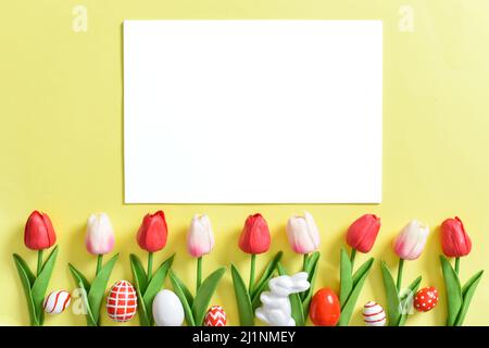 Sfondo con tulipani e uova di Pasqua su sfondo giallo con un foglio di carta bianco. Foto Stock