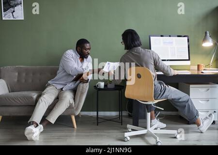 Minimo sparo a tutta lunghezza di due uomini d'affari che lavorano insieme sul progetto in ufficio contro il muro verde Foto Stock