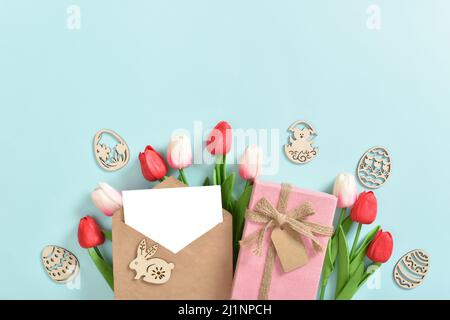 Un bouquet di tulipani con una cartolina, un regalo e uova di Pasqua in legno su sfondo blu. Foto Stock