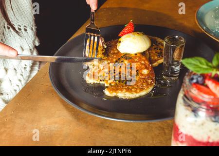 Un Closeup di pancake con fragole, un frutto della passione, e gelato servito su un piatto nero Foto Stock